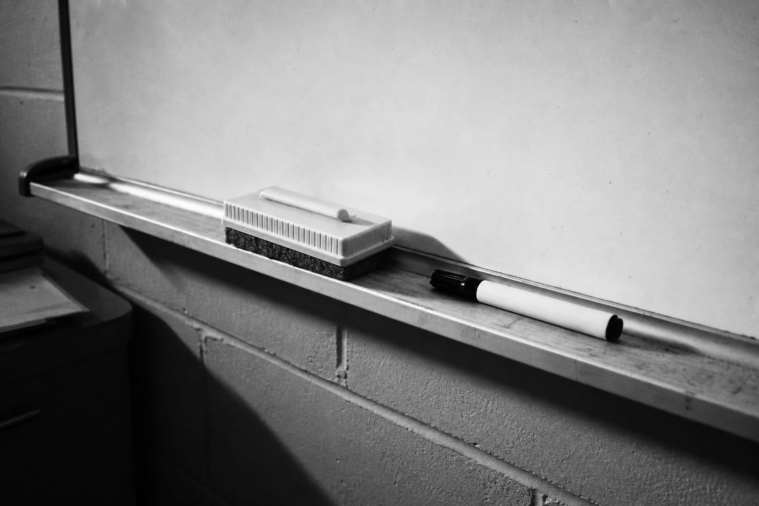 A whiteboard eraser and a dry-erase marker resting on the ledge beneath a blank whiteboard in a shop office