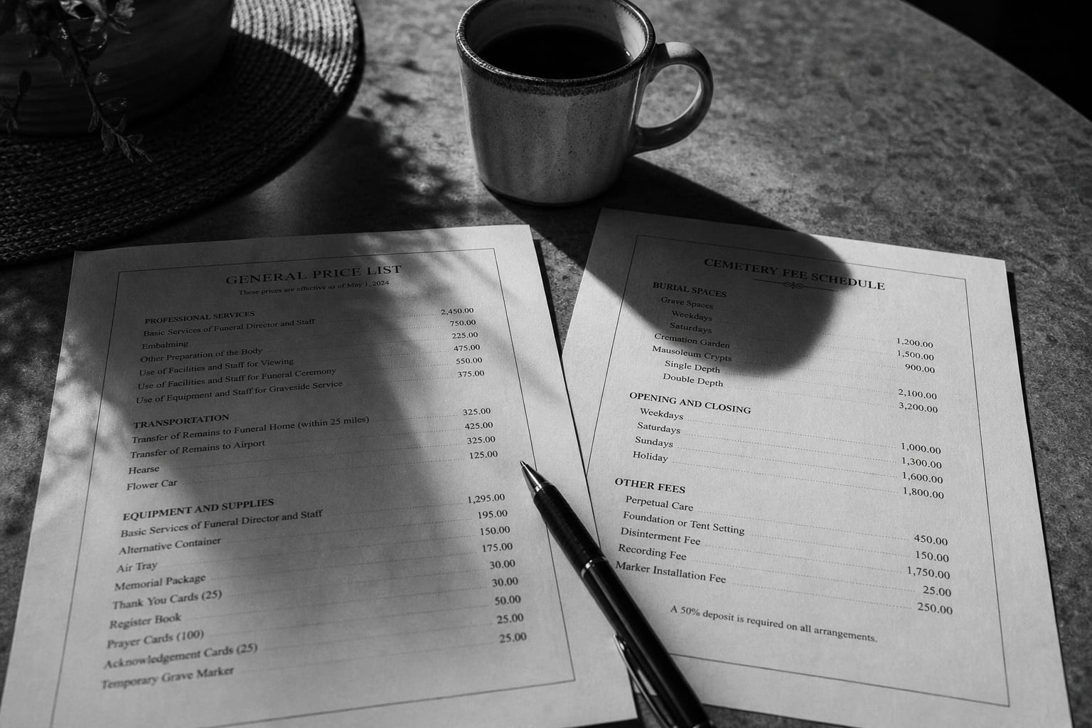 A printed itemized funeral general price list and a cemetery fee schedule lying side by side on a kitchen table with a pen and a mug