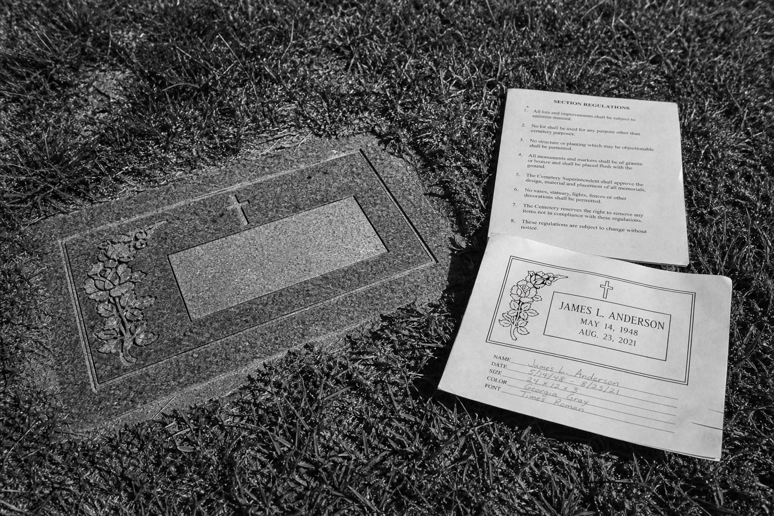 A flush granite grave marker set level with mown cemetery grass, with a printed page of cemetery section regulations and a monument dealer's inscription proo...