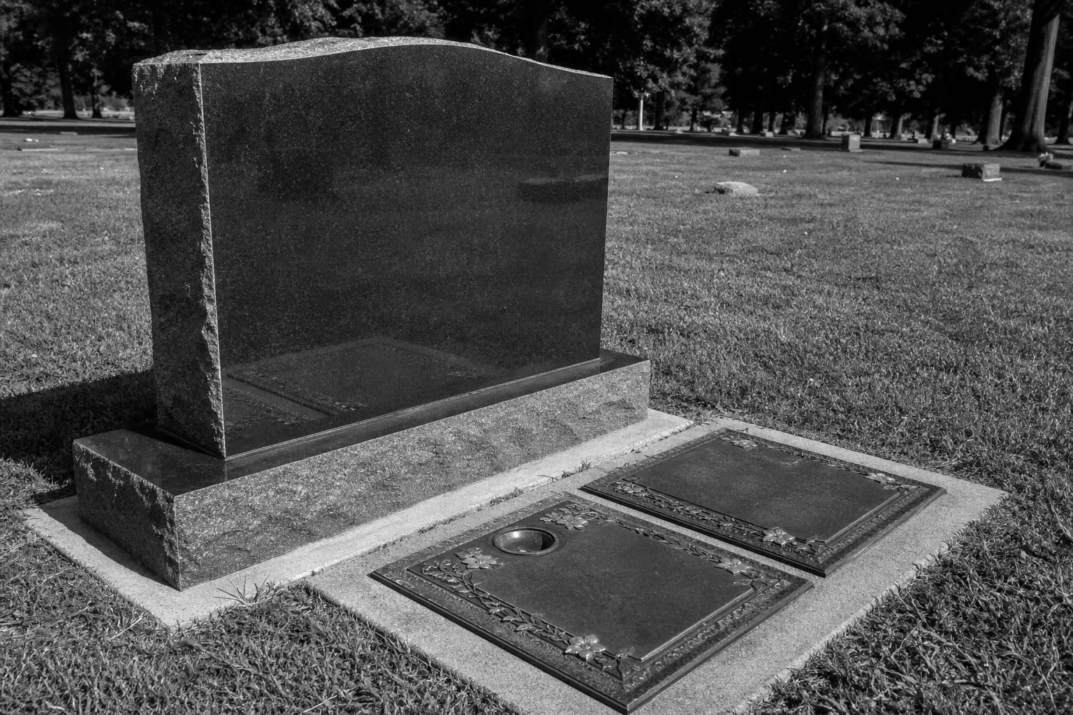 A granite upright monument with a polished front face standing beside flush bronze-on-granite markers in a cemetery lawn, with a concrete foundation edge vis...