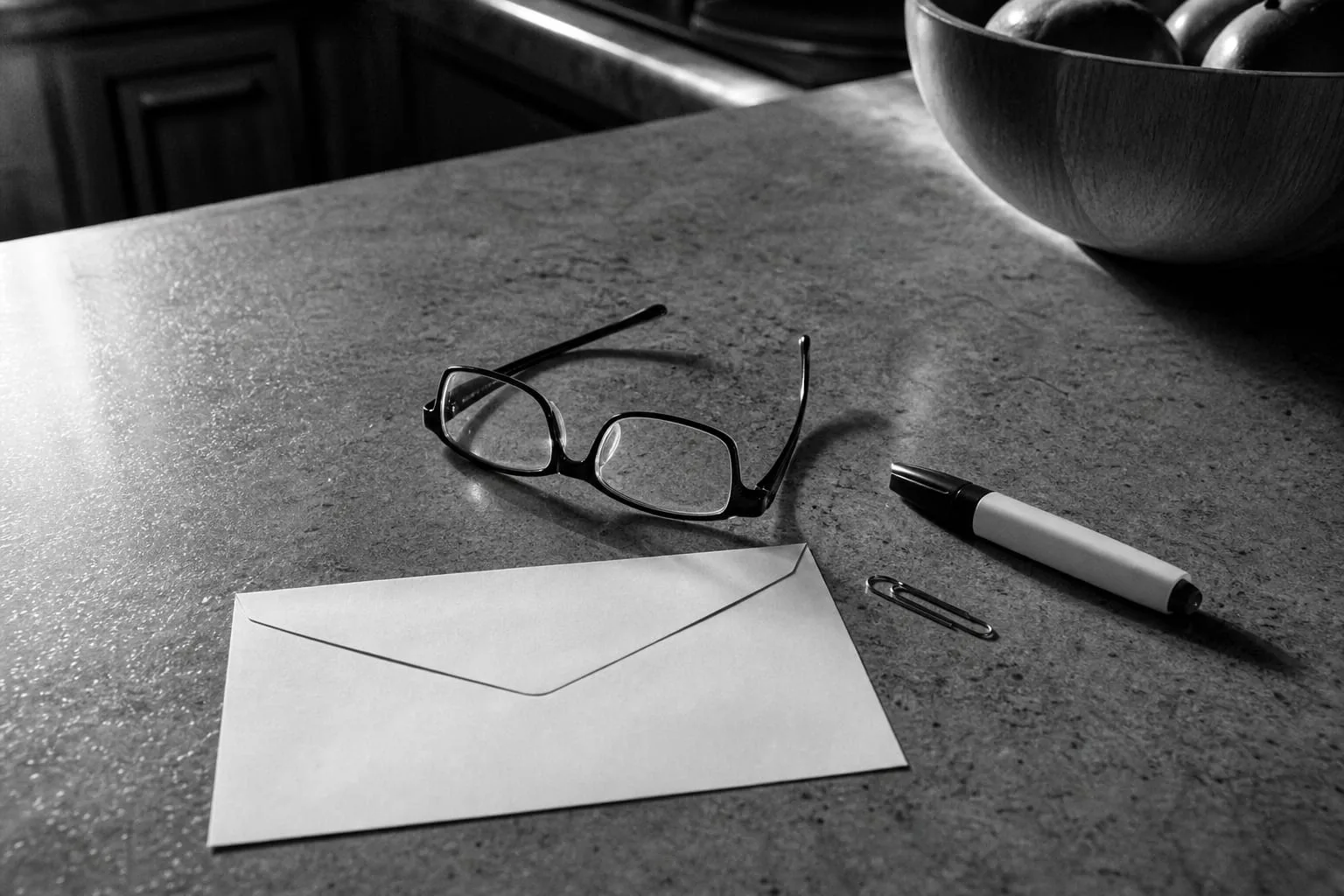 A kitchen counter with reading glasses, a highlighter and a paper clip resting beside a plain unmarked envelope